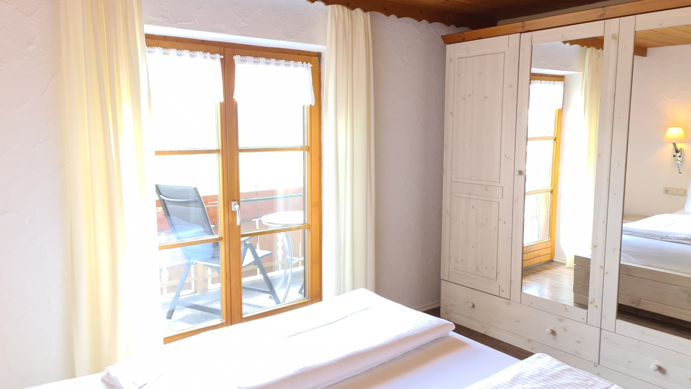 Das Doppelbett mit Kleiderschrank und Balkontüre zum Ostbalkon im Schafzimmer der Ferienwohnung Nebelhorn